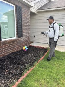 A Diamond Pest Solutions technician in Conway, AR, applying pest control treatment to the foundation of a house with a backpack sprayer.