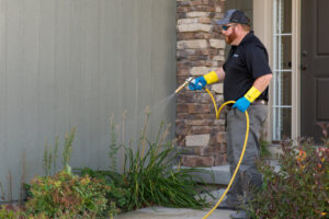 A KC Pest Experts technician spraying around a house foundation for pest control in Olathe, KS.