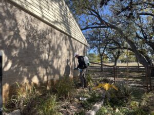 A Blessed Pest Control technician applying an exterior pest treatment to the foundation of a brick house in San Antonio, TX