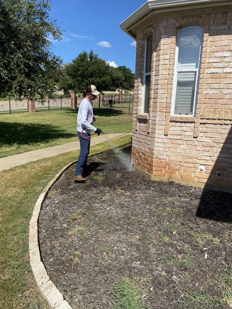 A Blue Line Pest Police technician spraying the perimeter of a house for pest control in Fort Worth, TX.