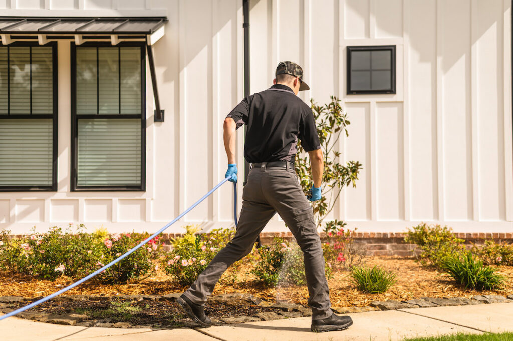 A pest control technician spraying liquid treatment along the perimeter of a house for The Pest Detective in Cleveland, OH.