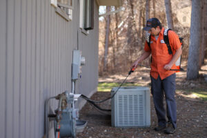 A technician spraying the perimeter of a house near an AC unit for pest control by Pest Free Rochester in Rochester, MN.