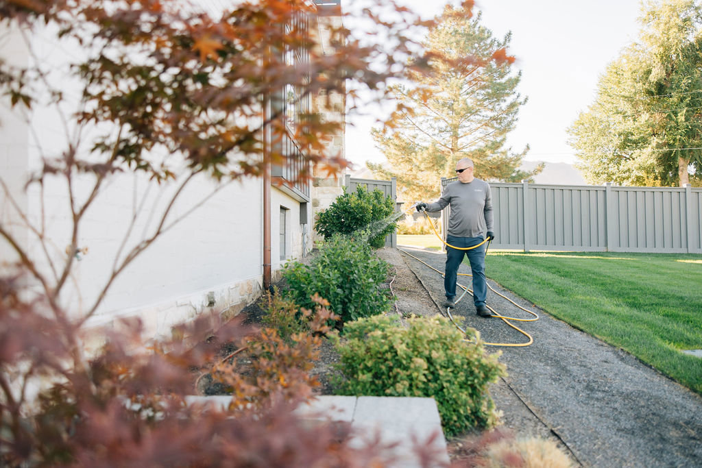 A technician spraying the perimeter of a house as part of pest control services by Thrive Pest Management in Sandy, UT