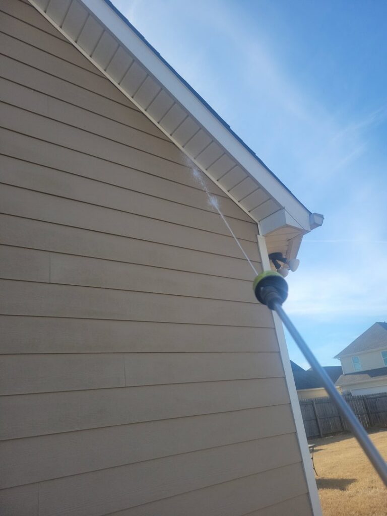 A technician from A Plus Pest Control spraying the siding of a house for pest management in Huntsville, AL.