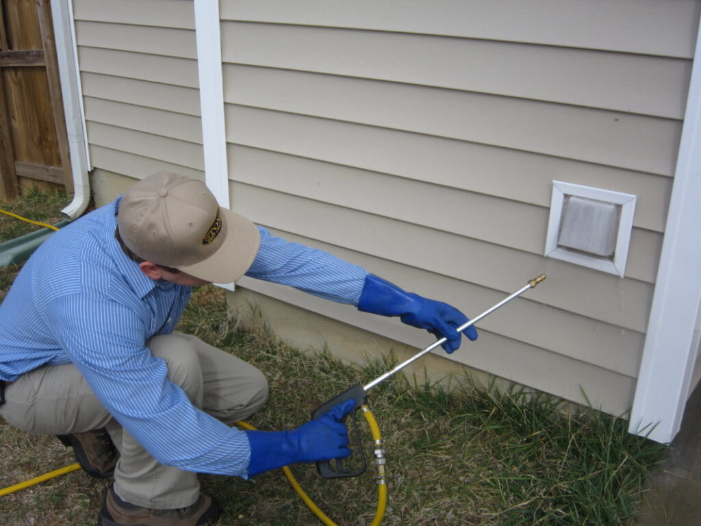 A Stomp Pest Control technician spraying around a house vent to prevent pest entry in Raleigh, NC.