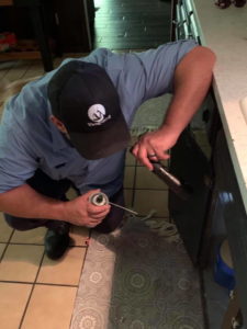 A pest control technician spraying inside a kitchen cabinet or appliance for Vanguard Pest Solutions in Oklahoma City, OK