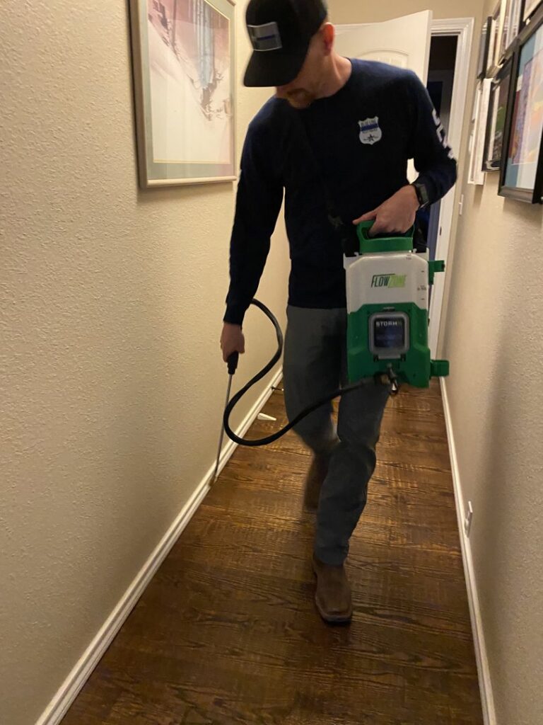 A Blue Line Pest Police technician spraying baseboards inside a home for pest control in Fort Worth, TX.