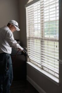 A Rumble Pest Solutions technician spraying an interior window frame during a pest control service in Springdale, AR.