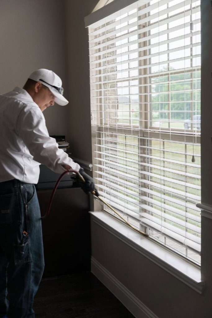 A Rumble Pest Solutions technician spraying an interior window frame during a pest control service in Springdale, AR.