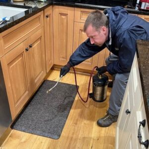 A Canady & Son Exterminating technician spraying for pests under kitchen cabinets during a service call in Wilmington, NC.