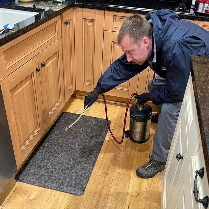 A Canady & Son Exterminating technician spraying for pests under kitchen cabinets during a service call in Wilmington, NC.