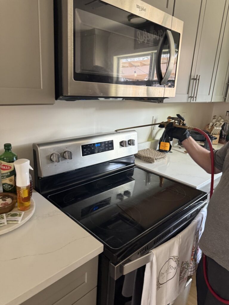 A Rosie's Pest Control technician applying treatment in a residential kitchen near a stove in Memphis, TN.