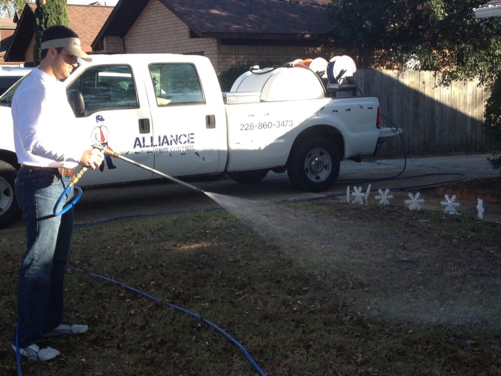A technician from Alliance Pest Control spraying a lawn with a hose from a service truck in Alliance, OH