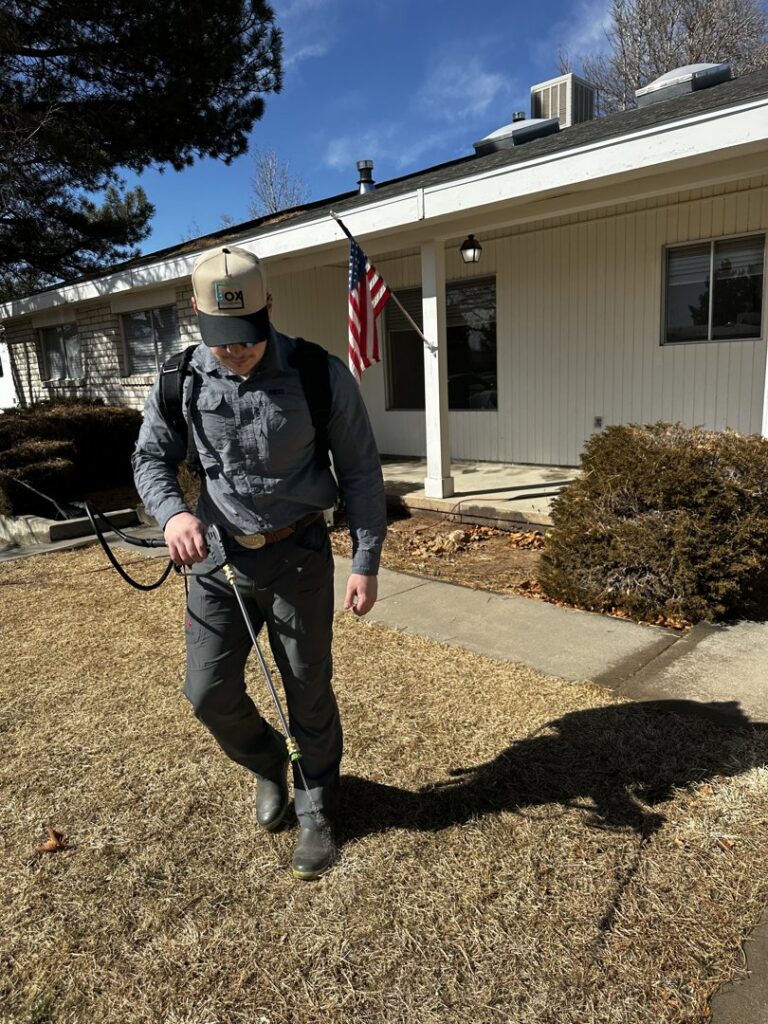 A Box Pest Control technician spraying a residential lawn for pest control in Farmington, NM.