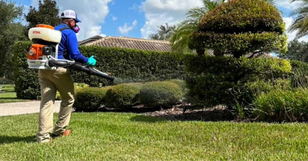 A Sorko Services technician applying pest control treatment to a lawn and bushes in Sanford, FL.
