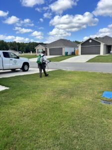 A Diamond Pest Solutions technician in Conway, AR, spraying a residential lawn as part of a pest control service, with a company truck nearby.
