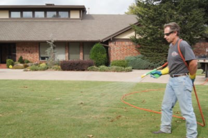 A pest control technician from Reliable Termite of OKC spraying a residential lawn for pest treatment in Oklahoma City, OK.