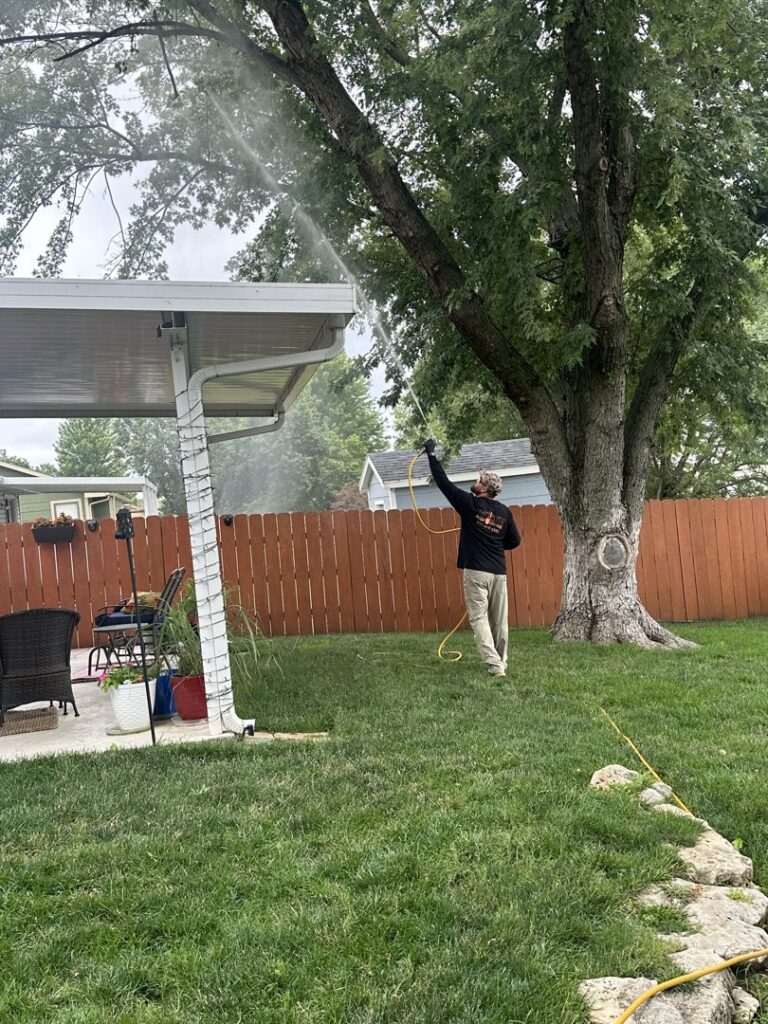 A pest control technician spraying under a patio cover and in a yard for pests by Elite Pest Control in Maple Grove, MN.