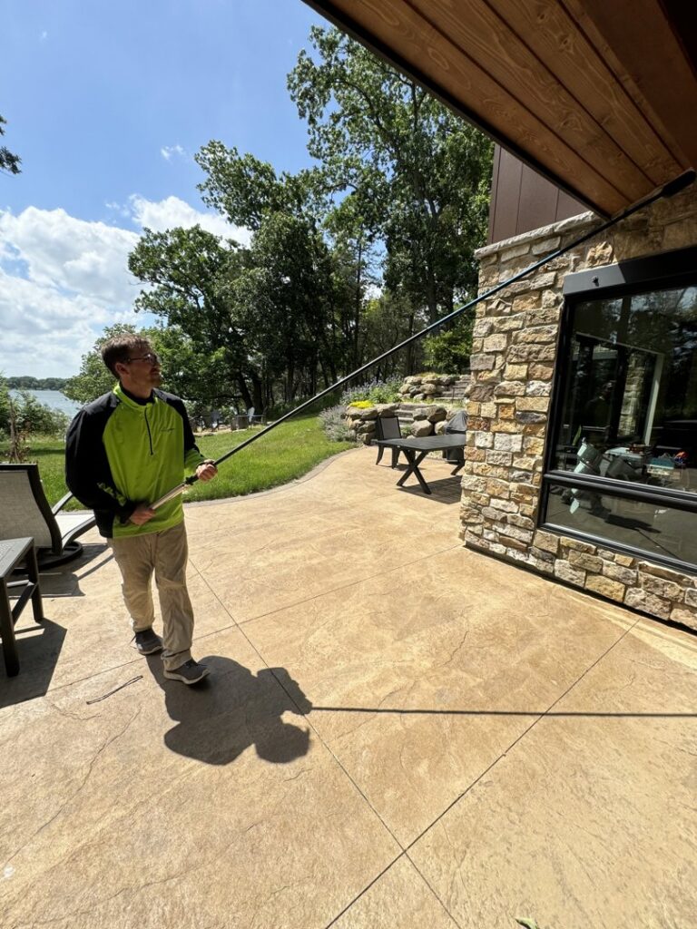 A Green Harmony technician performing pest control treatment near a patio and lake in Oconomowoc, WI.