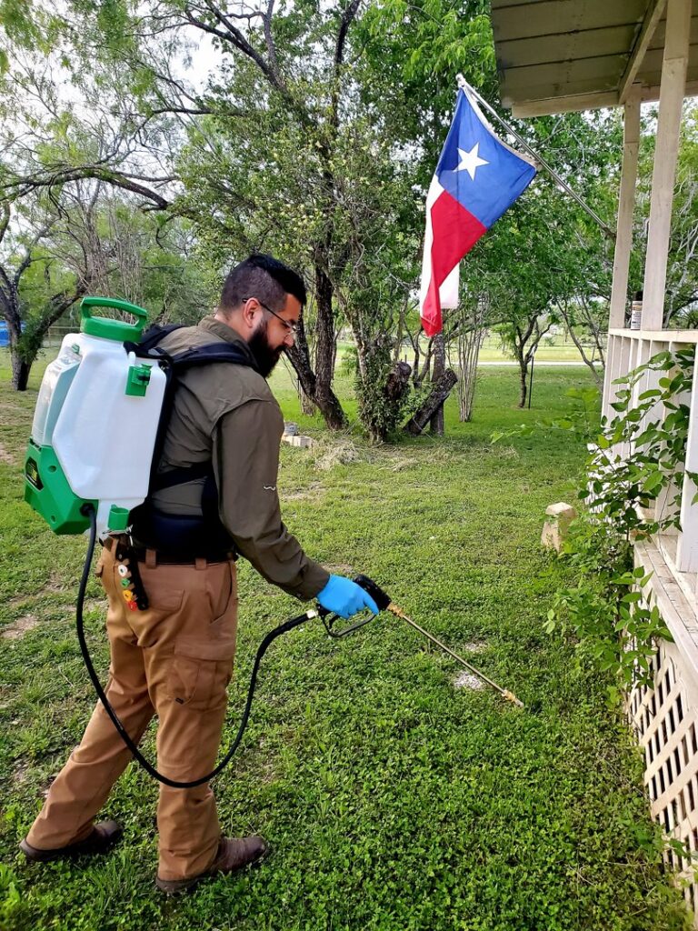 A technician from Rat King Pest Control spraying the perimeter of a house for pest control in San Antonio, TX.