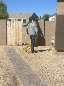 A C4 Pest Solutions technician pulling a hose to spray for pest control in a residential backyard in Wittmann, AZ.