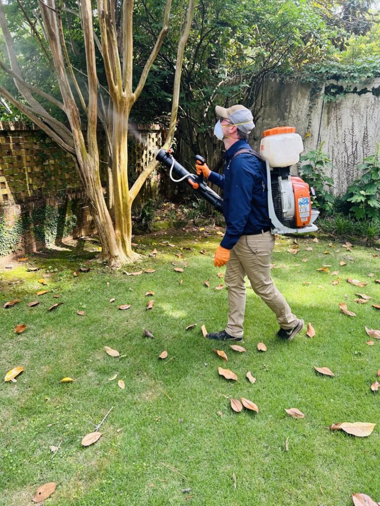 A technician from Athena Pest Control applying a pest control treatment with a backpack sprayer in a yard in Birmingham, AL.
