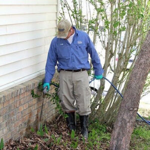 A technician spraying liquid pest treatment along a house foundation for Curry's Termite, Pest & Animal Control in Little Rock, AR