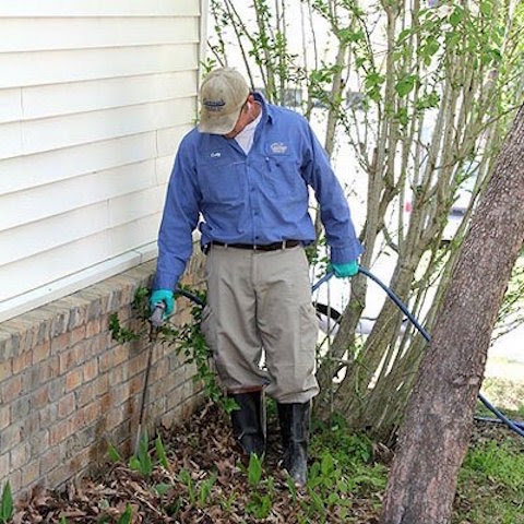 A technician spraying liquid pest treatment along a house foundation for Curry's Termite, Pest & Animal Control in Little Rock, AR
