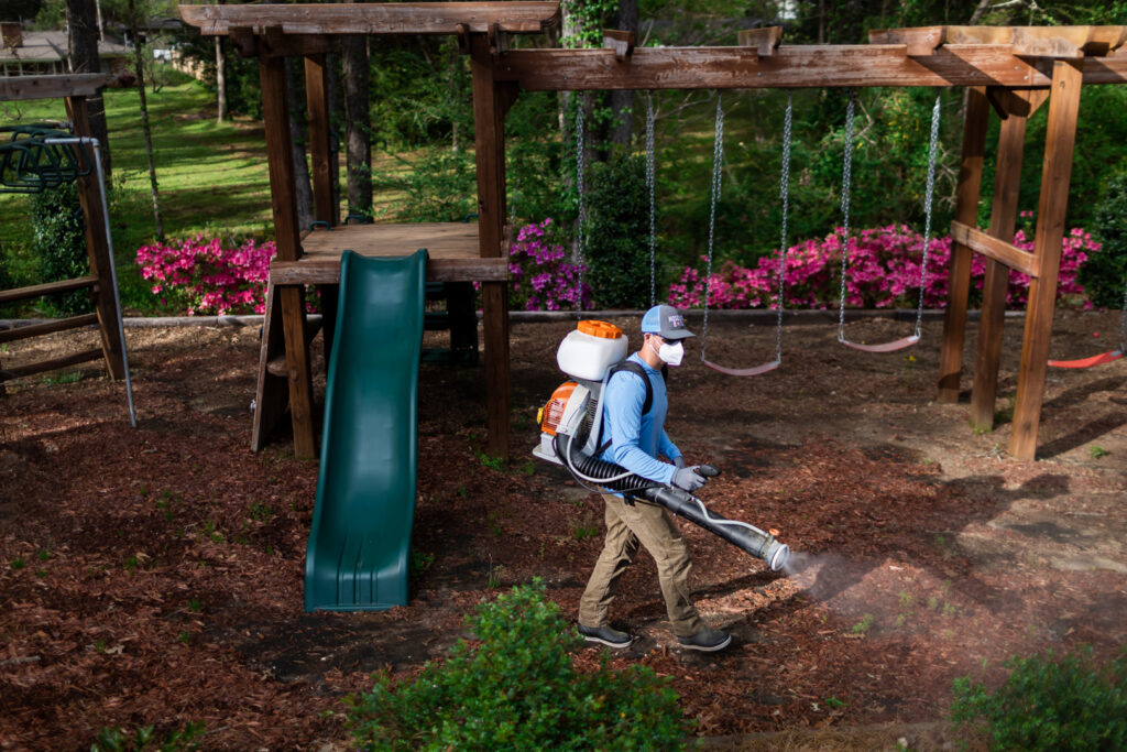 A Mosquito Boss technician spraying around a children's playground area for pest control in Brandon, MS