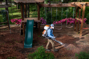A Mosquito Boss technician spraying around a children's playground area for pest control in Brandon, MS