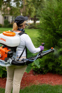 A Nature Spray Organics technician spraying shrubbery with a backpack sprayer in East Canton, OH.