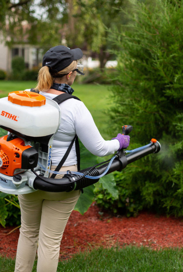 A Nature Spray Organics technician spraying shrubbery with a backpack sprayer in East Canton, OH.