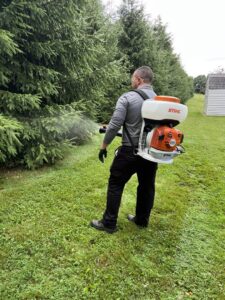 A Bye Bye Pest Solutions technician spraying trees and shrubs with a backpack sprayer for pest control in Hanover, PA.