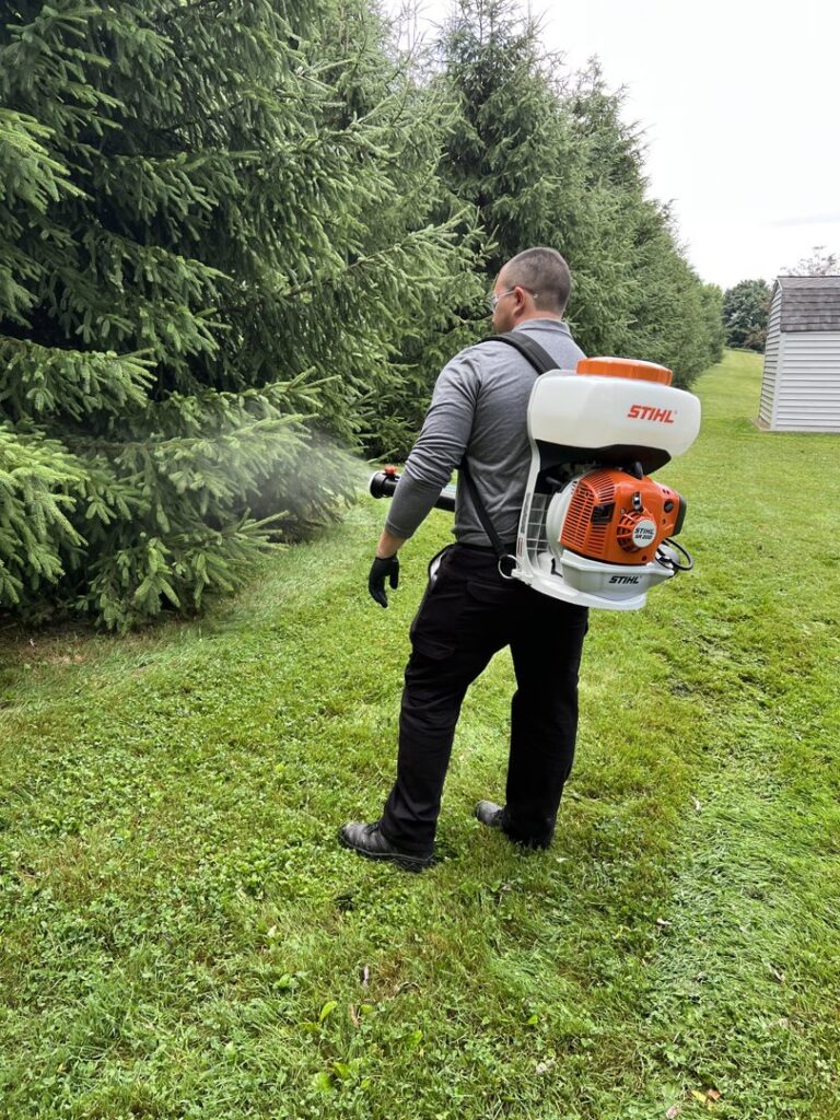 A Bye Bye Pest Solutions technician spraying trees and shrubs with a backpack sprayer for pest control in Hanover, PA.