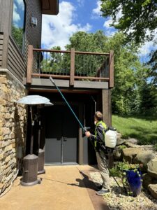 A Green Harmony technician performing pest control treatment under a residential deck in Oconomowoc, WI.