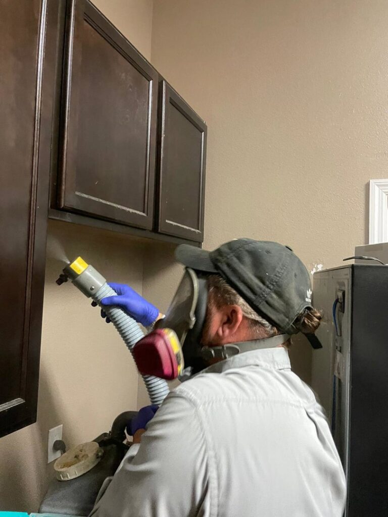An Avast Pest Control technician wearing a respirator mask while spraying under kitchen cabinets for pest treatment in Orlando, FL.