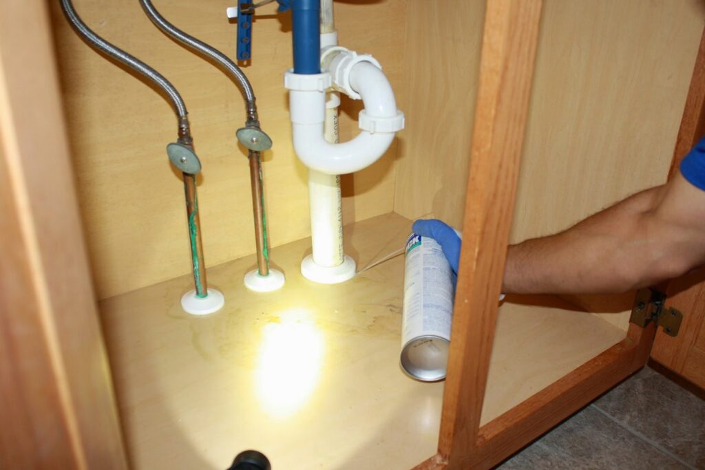 A Capital Pest Services technician spraying under a kitchen or bathroom sink for pests in Raleigh, NC.
