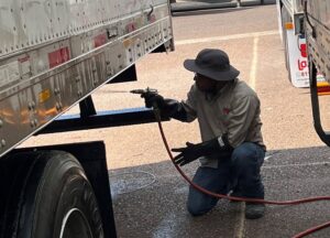 A Target Pest Control technician spraying under a large commercial trailer in Manchester, CT, performing pest treatment.