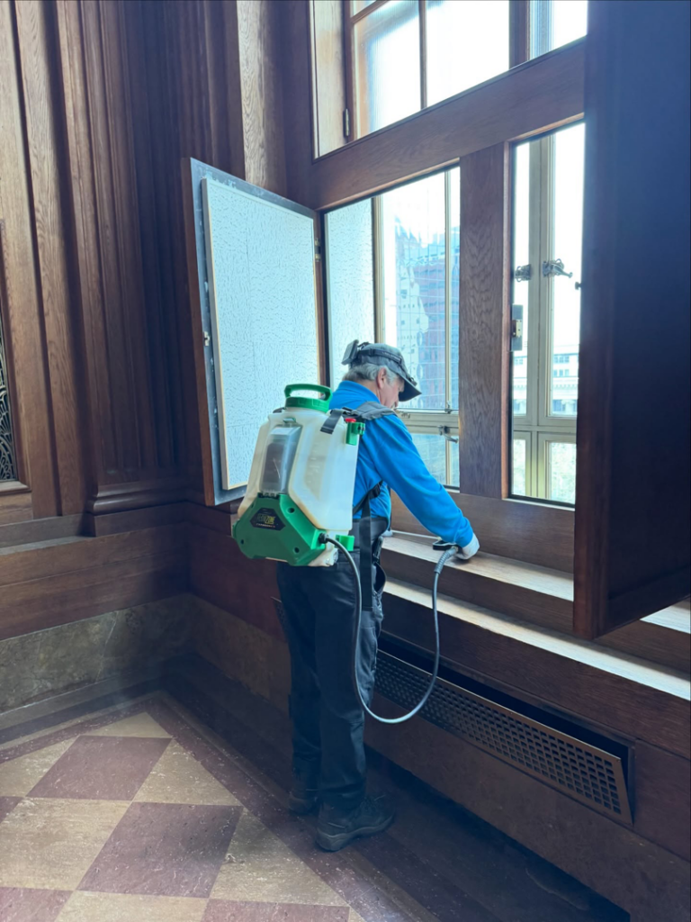 A Pest Lock, Inc. technician spraying near a window inside a commercial building for pest control in Vancouver, WA.