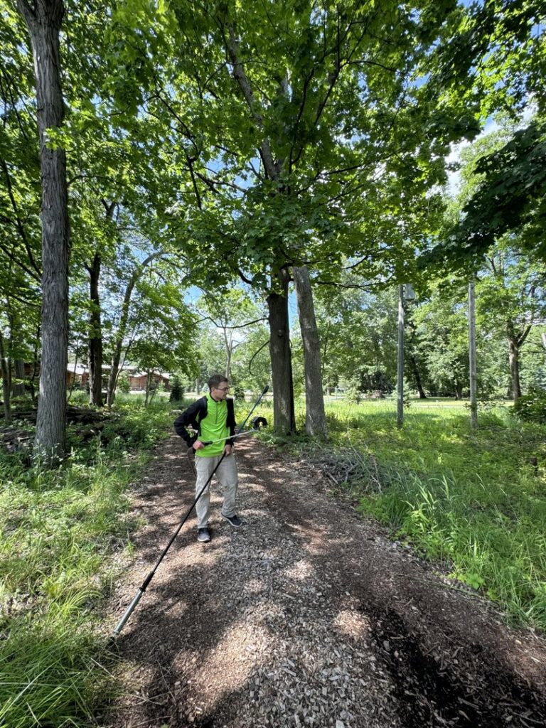 A Green Harmony technician applying pest control treatment in a wooded area for a client in Oconomowoc, WI.