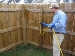 A Stomp Pest Control technician spraying a wooden fence to control pests around a property in Raleigh, NC.
