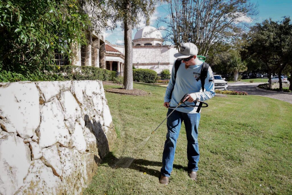 A Blessed Pest Control technician spraying a grassy area for perimeter pest control in San Antonio, TX