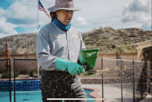 A Critter Gitters technician spreading pest control granules near a swimming pool in Lakeside, CA.