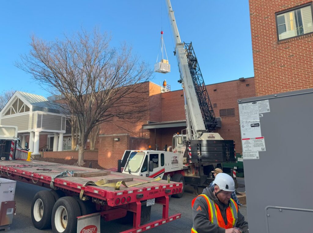A technician supervising the crane lift of a new HVAC unit onto a building for APEX HVAC Solutions LLC in Frederick, MD.