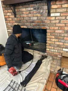 A SafeAir Duct & Chimney technician sweeping a residential fireplace with a power brush in Dallas, TX