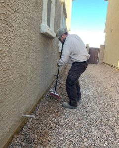 A technician sweeping the perimeter of a house, performing a task for Arizona Pest Control in Tucson, AZ.
