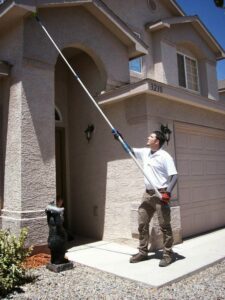 A pest control technician sweeping webs and nests from the eaves of a house for Advantage Pest & Weed Control in Rio Rancho, NM