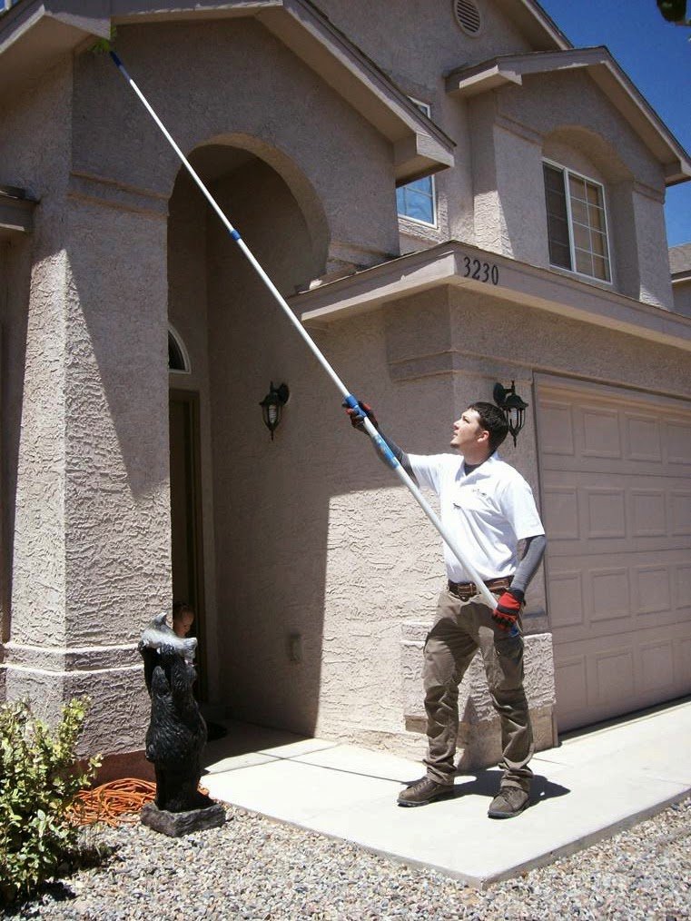 A pest control technician sweeping webs and nests from the eaves of a house for Advantage Pest & Weed Control in Rio Rancho, NM