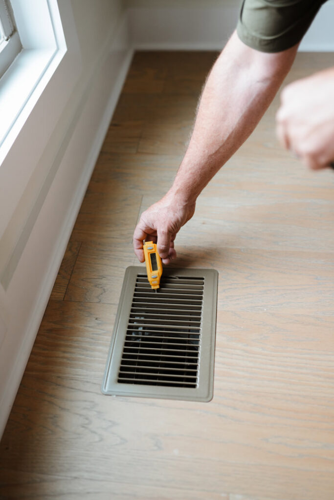 An HVAC technician testing the temperature at an indoor air vent with a sensor for Grace Heating & Air in Clarksville, TN.