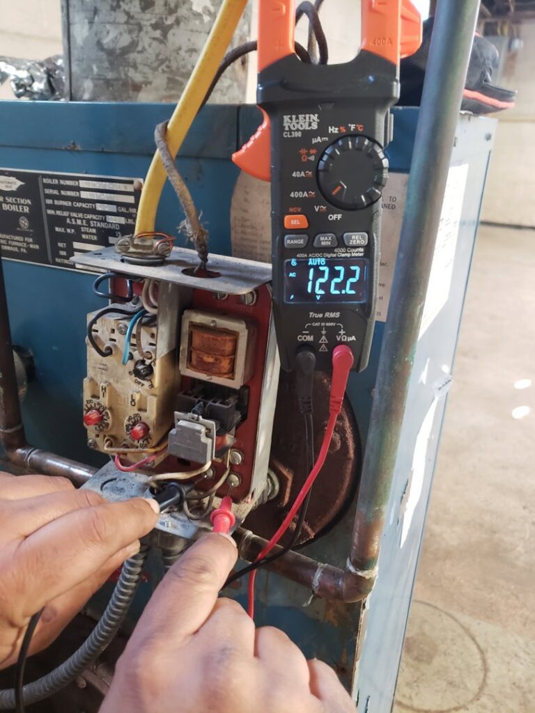 A technician using a multimeter to test a boiler control panel for JJJ Techs Heating and Cooling in Kinzers, PA.